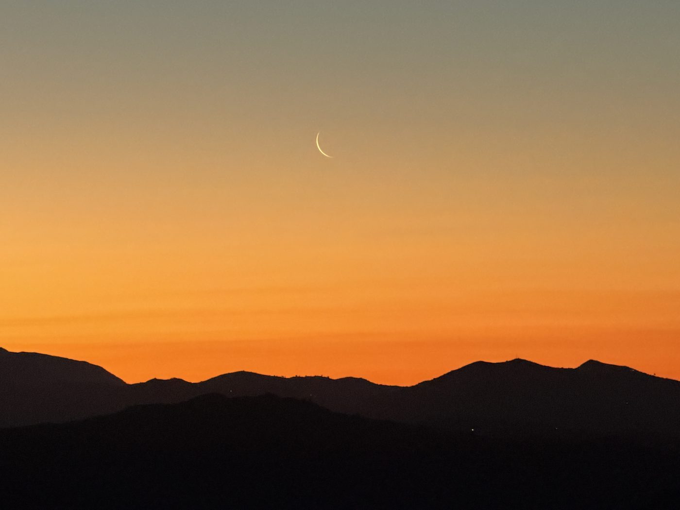 Maansikkel boven de bergkam in dieporanje avondrood